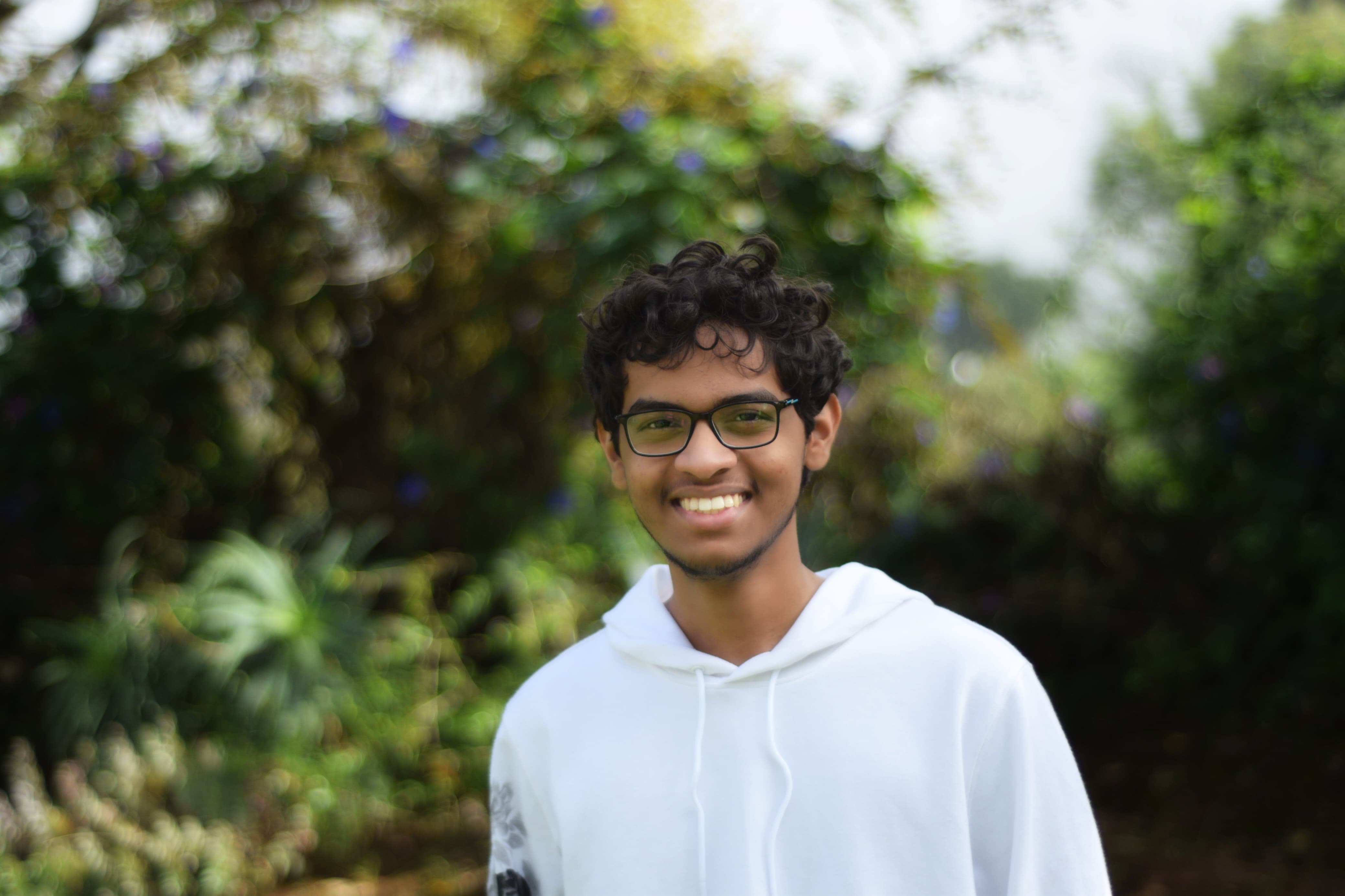 Photo taken by Advait of me standing in front of greenery. Background is blurry. I'm wearing a white hoodie.